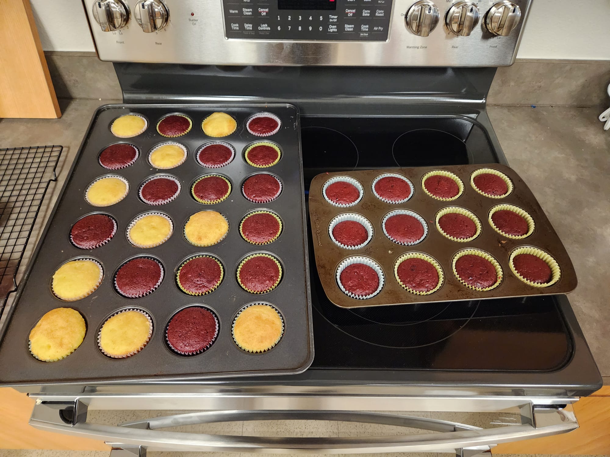 Freshly baked red velvet and vanilla cupcakes cooling in muffin pans